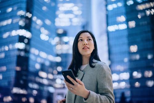 Woman holding smartphone in financial district with illuminated skyscrapers at night