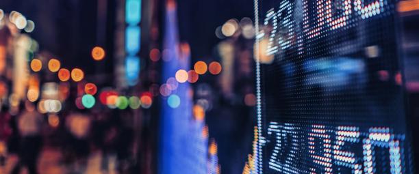 LED stock market ticker displaying financial data at night with city lights in the background