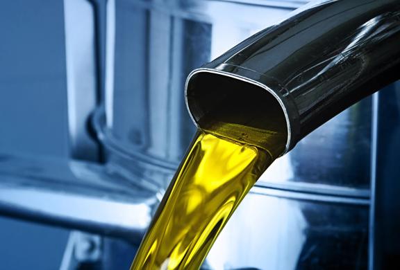 Close-up of cooking oil being poured from a stainless steel spout into a container.