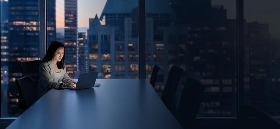Woman working late at night in an office with city view.