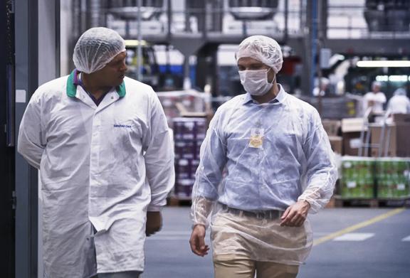 Two men walking through a processing facility wearing protective clothing and hair coverings