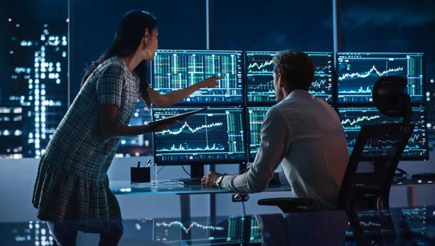 Investment professionals exchanging ideas in front of financial market dashboards