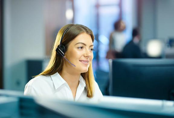Smiling female customer service representative wearing a headset, working in a modern office environment.