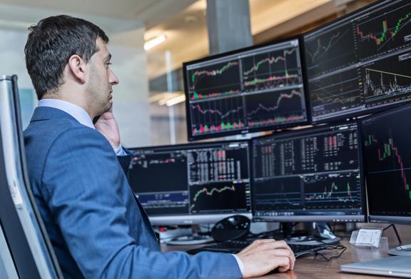 Stock trader in a suit analyzing multiple monitors displaying financial charts and market data in an office