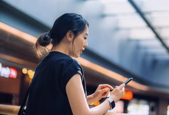 Young professional woman using a smartphone in a modern indoor space, representing mobile connectivity and digital communication.

