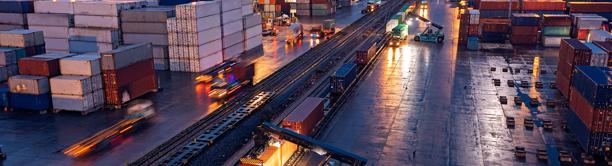 Intermodal freight terminal with containers, trucks, and cargo handling equipment at dusk