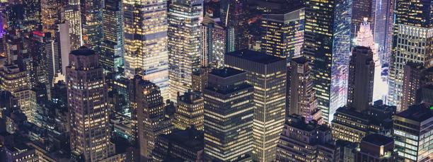 Nighttime aerial view of a dense city skyline with illuminated skyscrapers, symbolizing financial hubs and global commerce.
