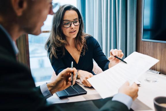 Mulher e homem em reunião de negócios, analisando e discutindo um documento contratual com anotações.