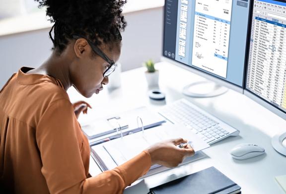 Woman studying folder with computer screen behind