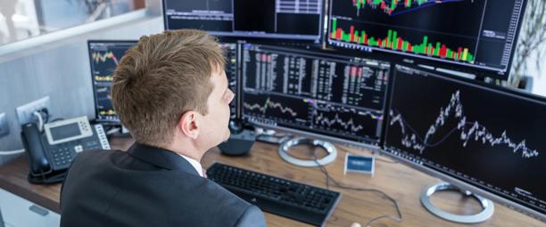 Male trader monitoring multiple financial charts and data screens