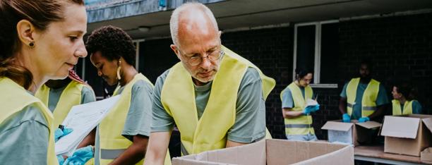 A group of volunteers wearing yellow vests and gloves are packing donation boxes in a community service event.
