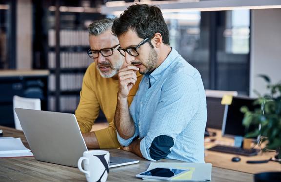 Two professionals collaborating over a laptop in a modern office environment

