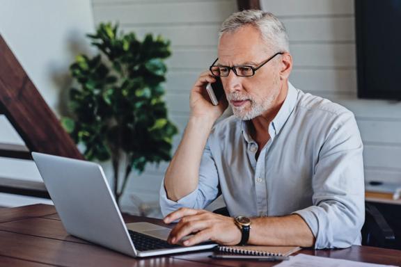 Man speaking on phone while working on laptop