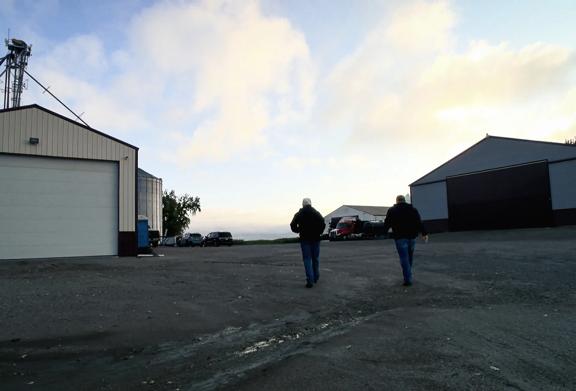 Two farmers walking between agricultural buildings on a family farm