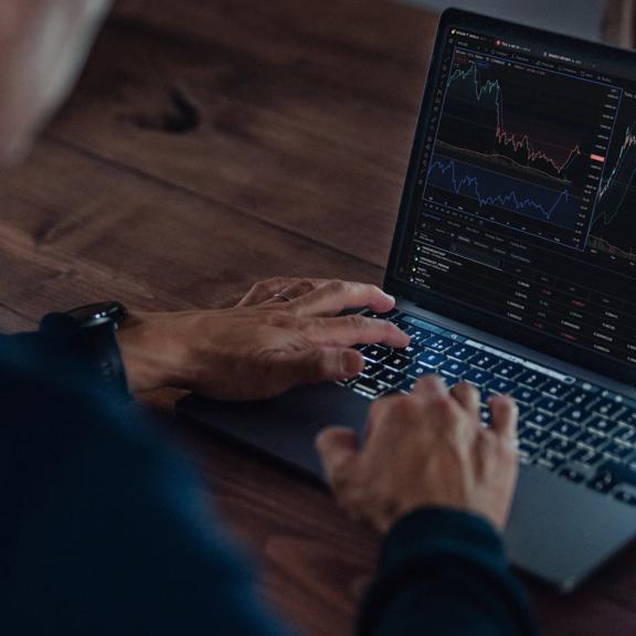 Trader using a laptop to monitor financial markets and live price charts.