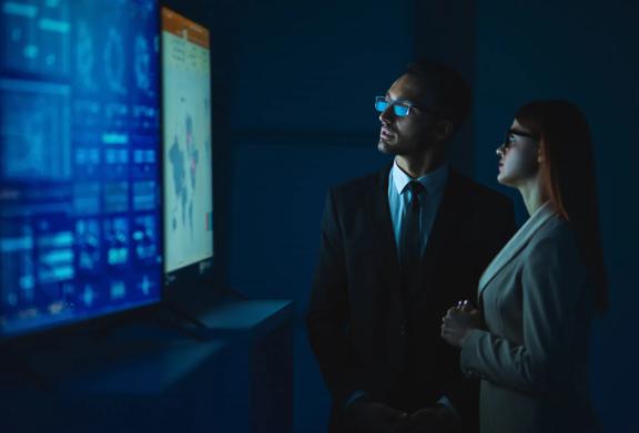 Man and woman looking at large screens in dark room
