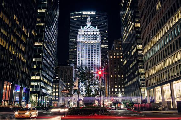 Nighttime view of New York City skyline with illuminated skyscrapers and traffic on Fifth Avenue.