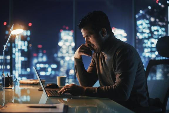Market analyst monitoring financial data and global market activity from an office overlooking a city skyline.