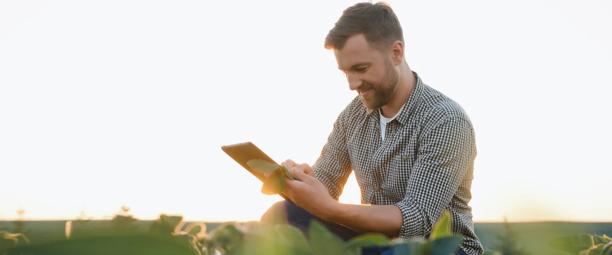 Homem usando um tablet ao ar livre em um campo durante o pôr do sol.