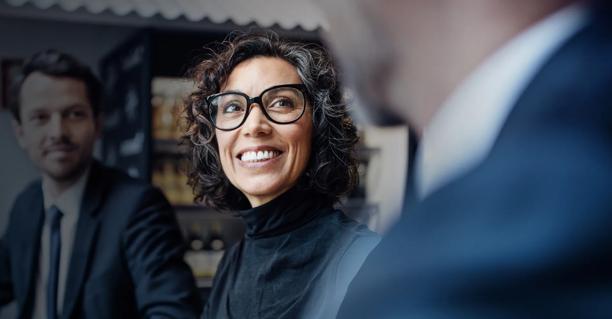 Uma mulher profissional sorridente usando óculos cercada por colegas profissionais