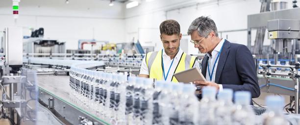 Two professionals inspecting bottled water production line in a modern factory