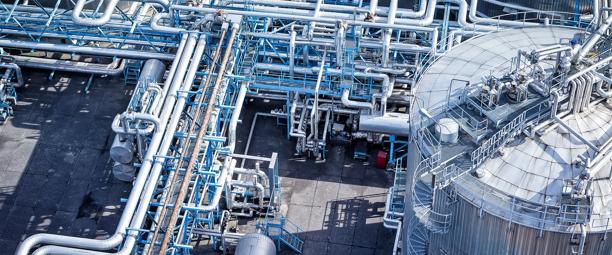 Vista aérea de uma instalação industrial com tubulações interconectadas e tanques de armazenamento, mostrando uma complexa infraestrutura de fabricação