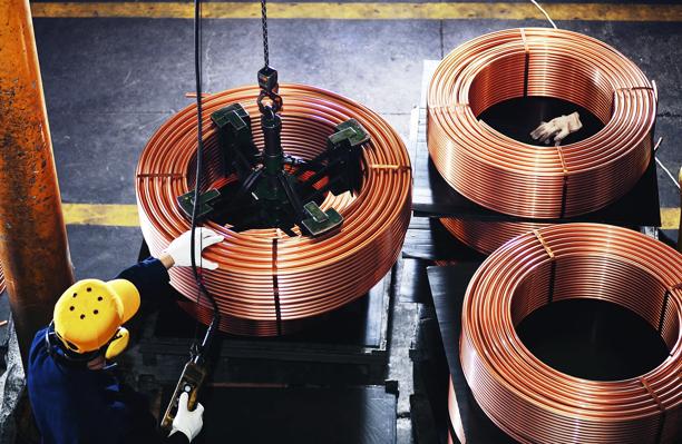Worker operating machinery to move large copper coils in an industrial facility, representing copper production and commodities logistics.
