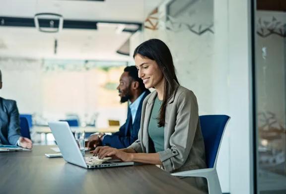 Profissional digitando em um notebook em uma mesa de reunião com colegas próximos