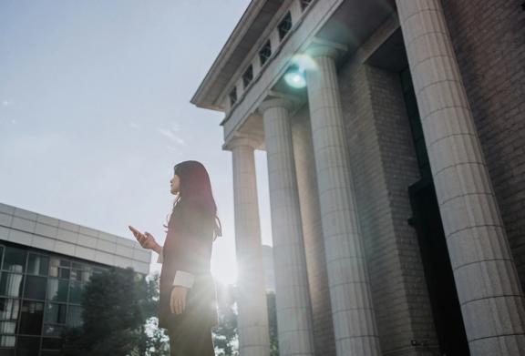 Businesswoman standing outside a neoclassical office building using a smartphone