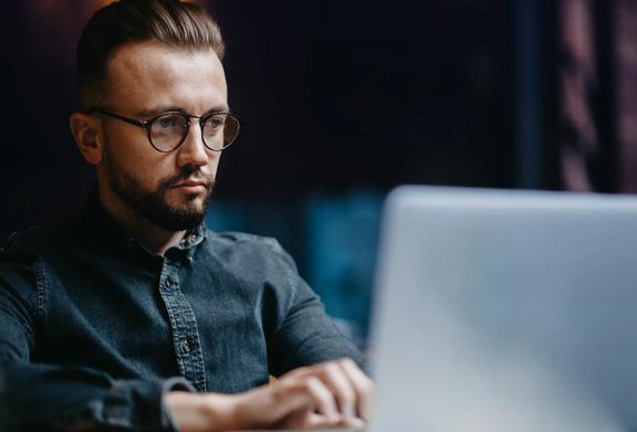 Concentrated man working on a laptop, analyzing data or performing research in a professional environment.