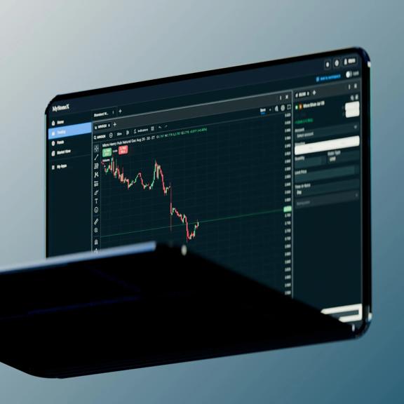 Digital trading platform displayed on a widescreen monitor featuring a live financial chart, market data tools, and technical analysis indicators against a blue gradient background, representing online trading and market analysis.