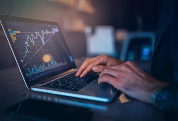 Hands typing on laptop with screen showing financial chart