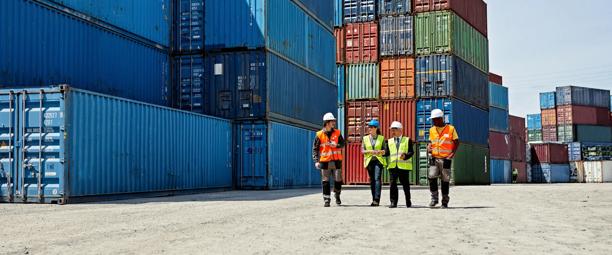 Trabalhadores inspecionando contêineres de carga em um pátio de expedição.