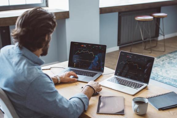 Broker sitting at a desk using two laptops to analyze the financial markets