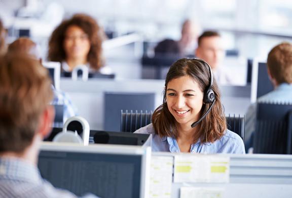 Smiling customer service representative wearing a headset in a busy call center office