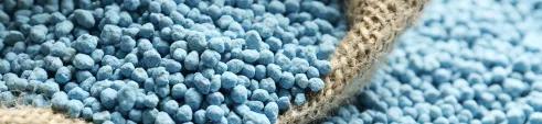 Fertilizante granulado azul sendo aplicado para melhorar a produtividade agrícola.