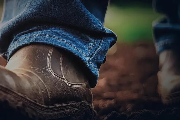 Close-up of worn work boots on soil, symbolizing hard work and connection to the land in agriculture.