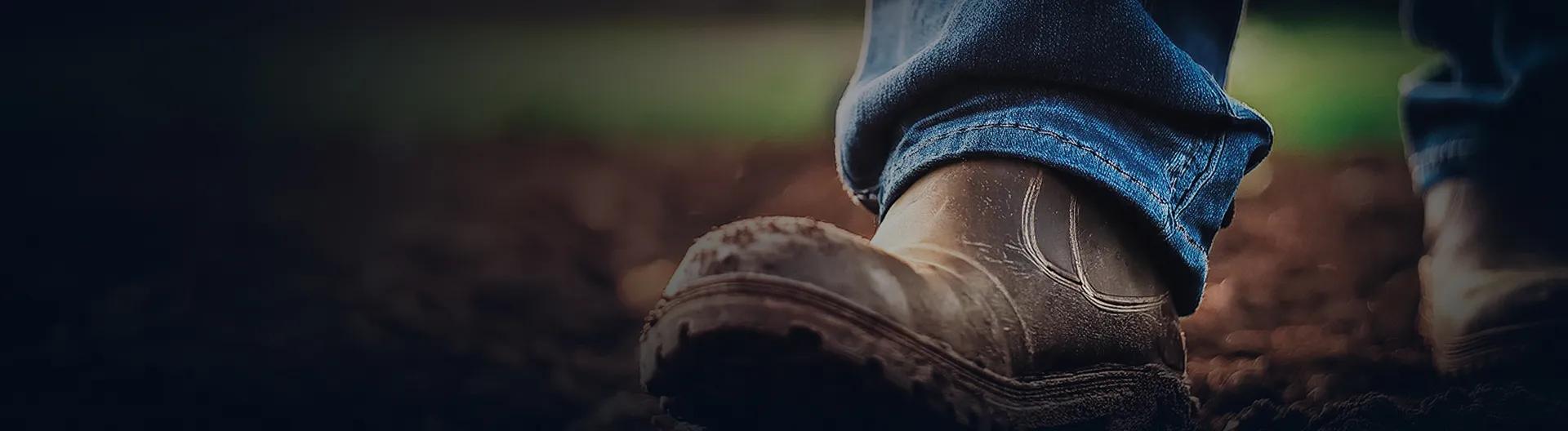Close-up of worn work boots on soil, symbolizing hard work and connection to the land in agriculture.