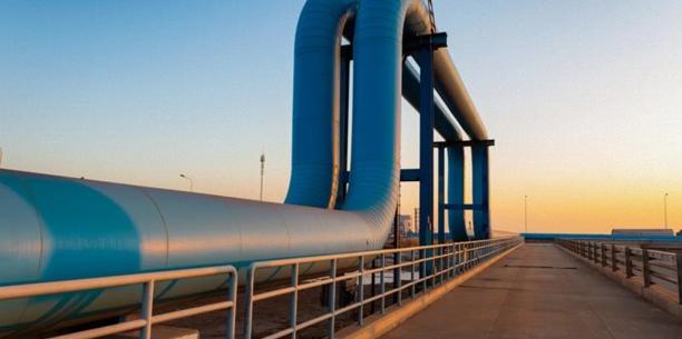 Industrial energy pipeline facility with large metal pipes extending towards the horizon at sunset.
