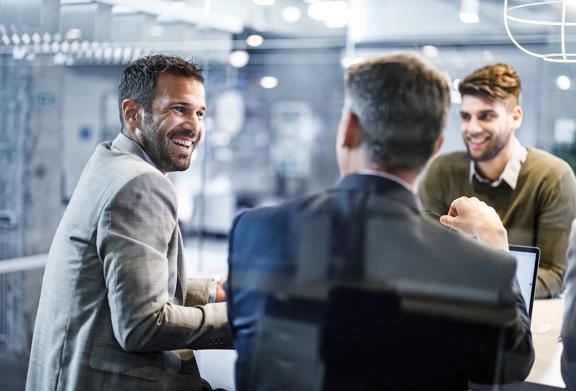 Group of professional men in business attire having a lively discussion in a modern office meeting room.