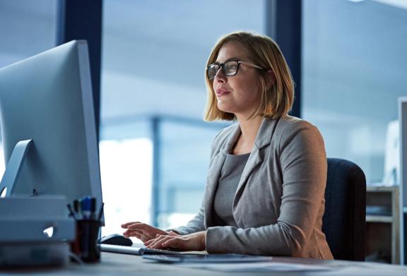 Professional woman in glasses working at a desktop computer in a modern office setting