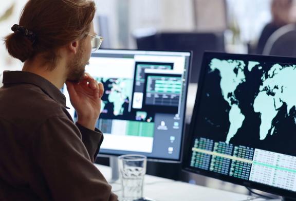 Analyst reviewing global data and statistics on multiple computer screens