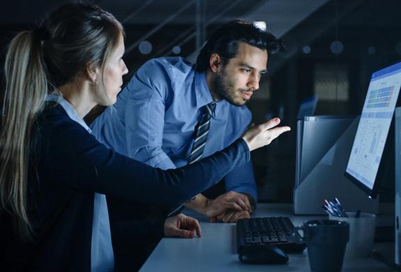 Two business professionals analyzing data on a desktop computer in a dimly lit office