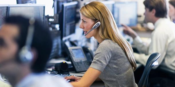 Customer support professionals working at computer workstations with headsets, providing trading and financial services assistance.