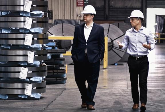 Two men wearing safety helmets walking through a metals warehouse