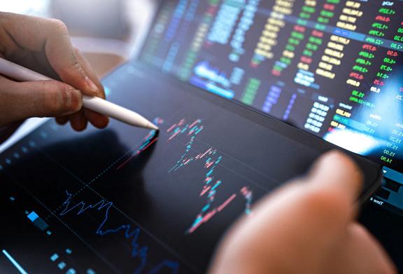 Close-up of a person using a stylus on a tablet to analyze stock market data and financial charts