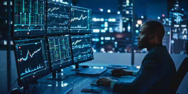 Profissional monitorando dados de mercado financeiro e gráficos de negociação em várias telas.