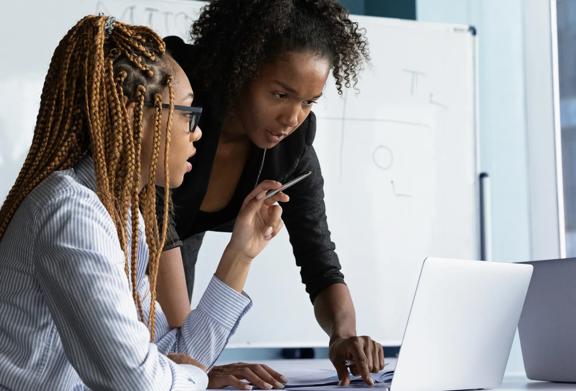 Two women collaborating on a project while reviewing documents and laptop data in an office