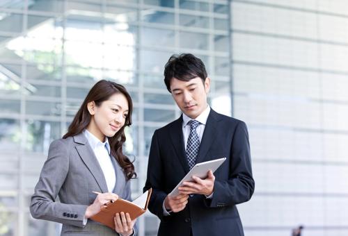 明るくモダンなオフィスで、テーブルを囲んでノートパソコンを使いながら仕事の話し合いをしているグループ。