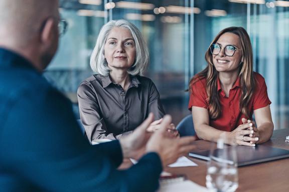 Três profissionais em mesa de reunião, dois homens e uma mulher, discutindo ideias e estratégias em escritório moderno.